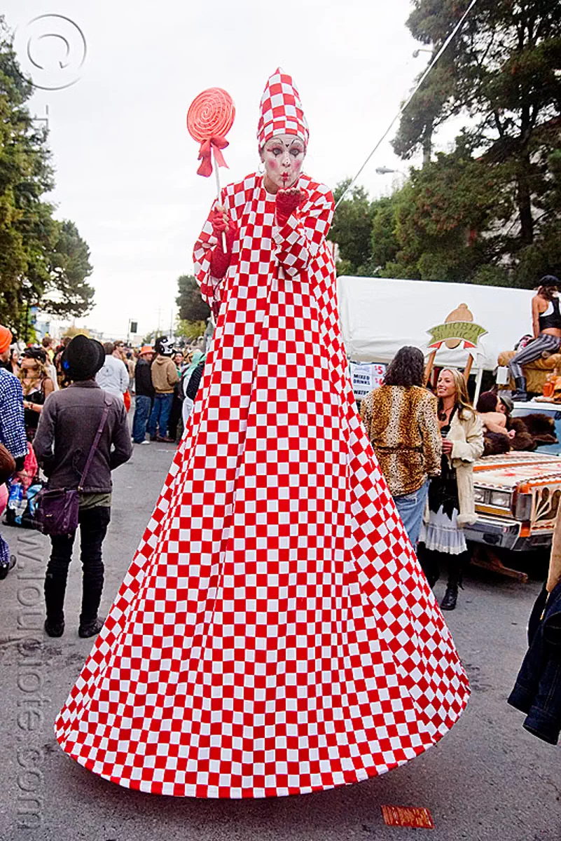 red and white stiltwalker with giant lollipop, burning man decompression, checkered, clown, costume, jesster, red lollipop, stilts, stiltwalking, stock photo