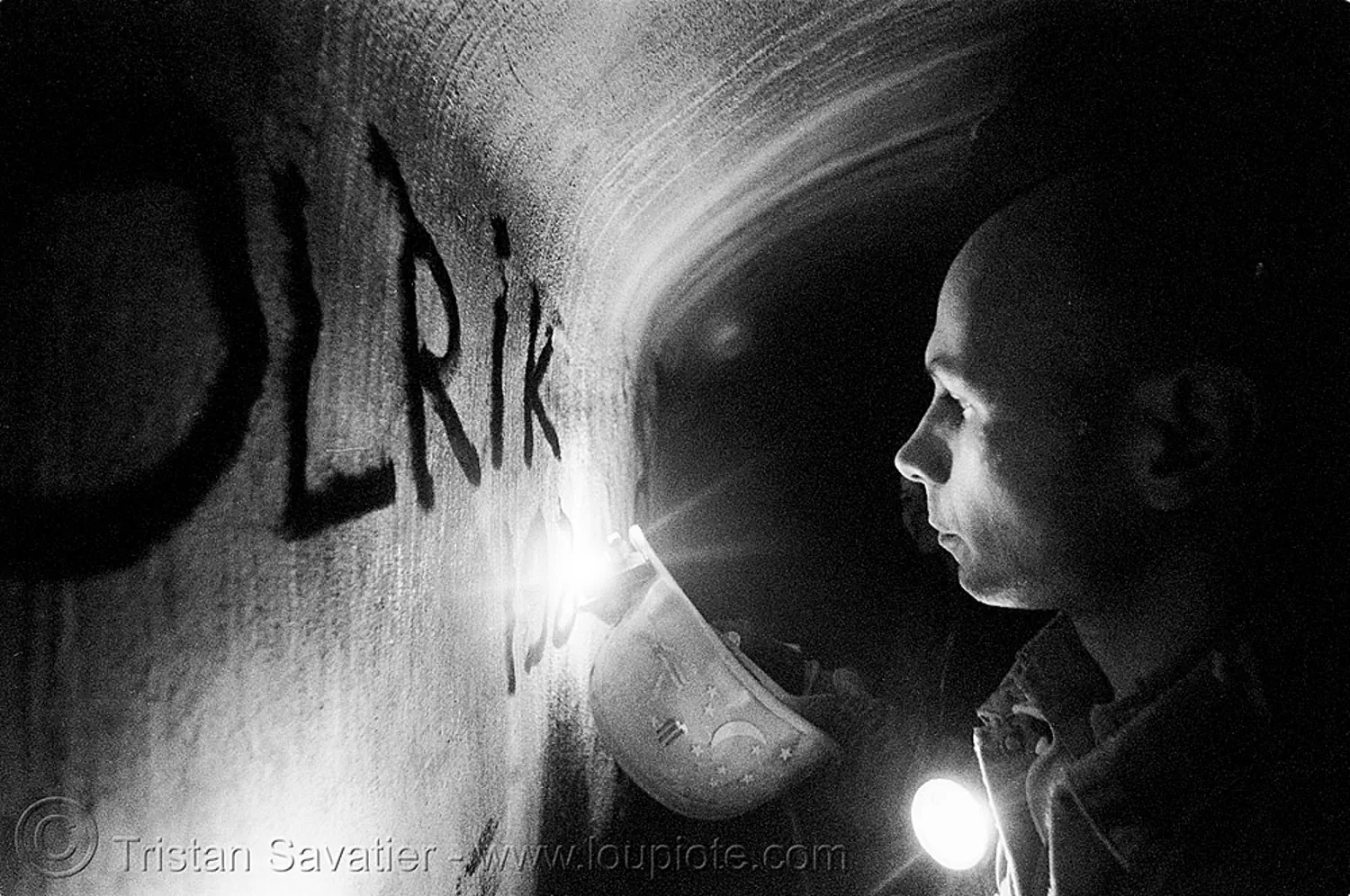 urban caver olrik writing on concrete wall of a utility tunnel with a carbide lamp (paris), acetylene, catacombs of paris, cave, caving, gallery, graffiti, p3200tmz, safety helmet, shadow, spelunking, tag, tmax, trespassing, underground quarry, urban exploration, stock photo
