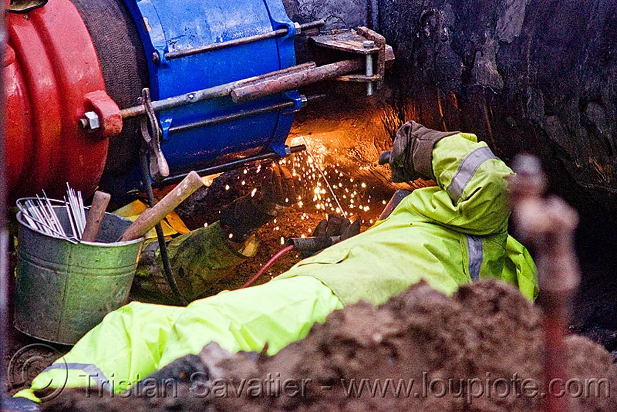 arc welding - utility worker fixing broken water main (san francisco), bucket, construction workers, contractor, electrodes, hetch hetchy water system, infrastructure, reflector vest, repairing, safety helmet, safety vest, sfpuc, sink hole, sparks, utility crew, utility workers, water department, water pipe, welder, stock photo