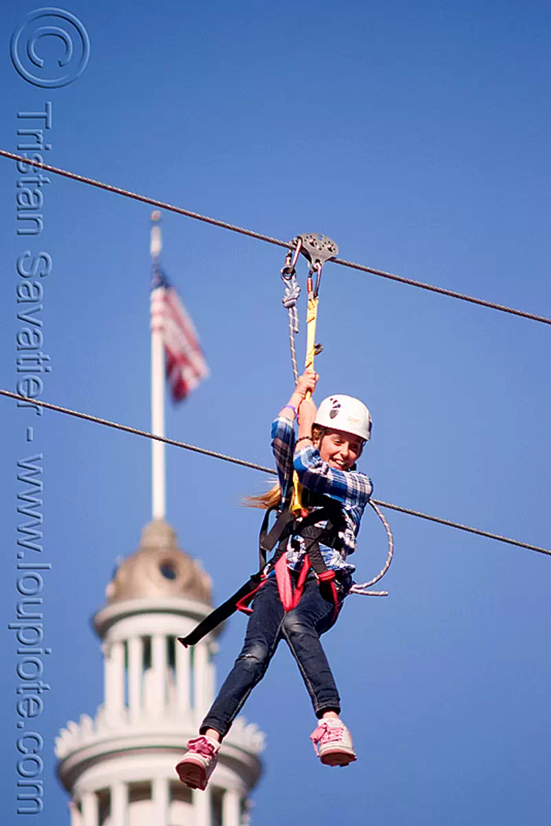 zip-line over san francisco, adventure, american flag, blue sky, cable line, cables, campanil, child, climbing helmet, clock tower, embarcadero tower, extreme sport, fast, ferry building, gear, hanging, harness, justin herman plaza, kid, mountaineering, moving, speed, steel cable, trolley, tyrolienne, urban, zip line, ziptrek, stock photo