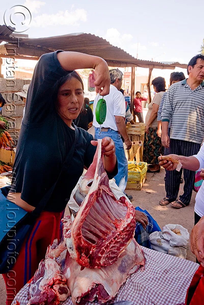 weighing a cut of llama meat (argentina), butcher, carnaval, carnival, market, meat shop, noroeste argentino, quebrada de humahuaca, raw meat, ribs, spring weighing scale, street vendor, weighting scale, stock photo