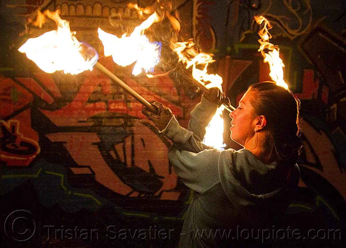 savanna spinning fire staffs, crossed arms, double staff, fire dancer, fire dancing, fire performer, fire spinning, fire staves, flame, graffiti, night, wall, stock photo