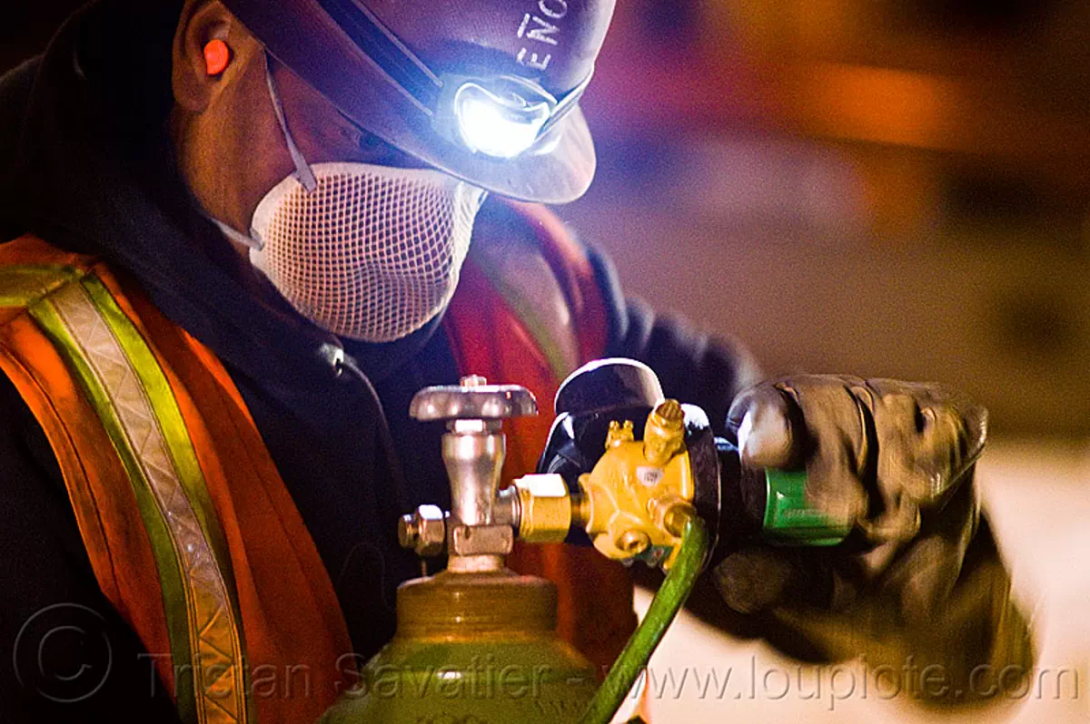 oxygen tank valve, dust mask, face-mask, headlamp, headlight, light rail, man, muni, night, ntk, oxy-acetylene, pressure gauge, railroad construction, railroad tracks, rails, reflective vest, regulator, safety glasses, safety gloves, safety helmet, safety vest, san francisco municipal railway, track maintenance, track work, welder, worker, stock photo