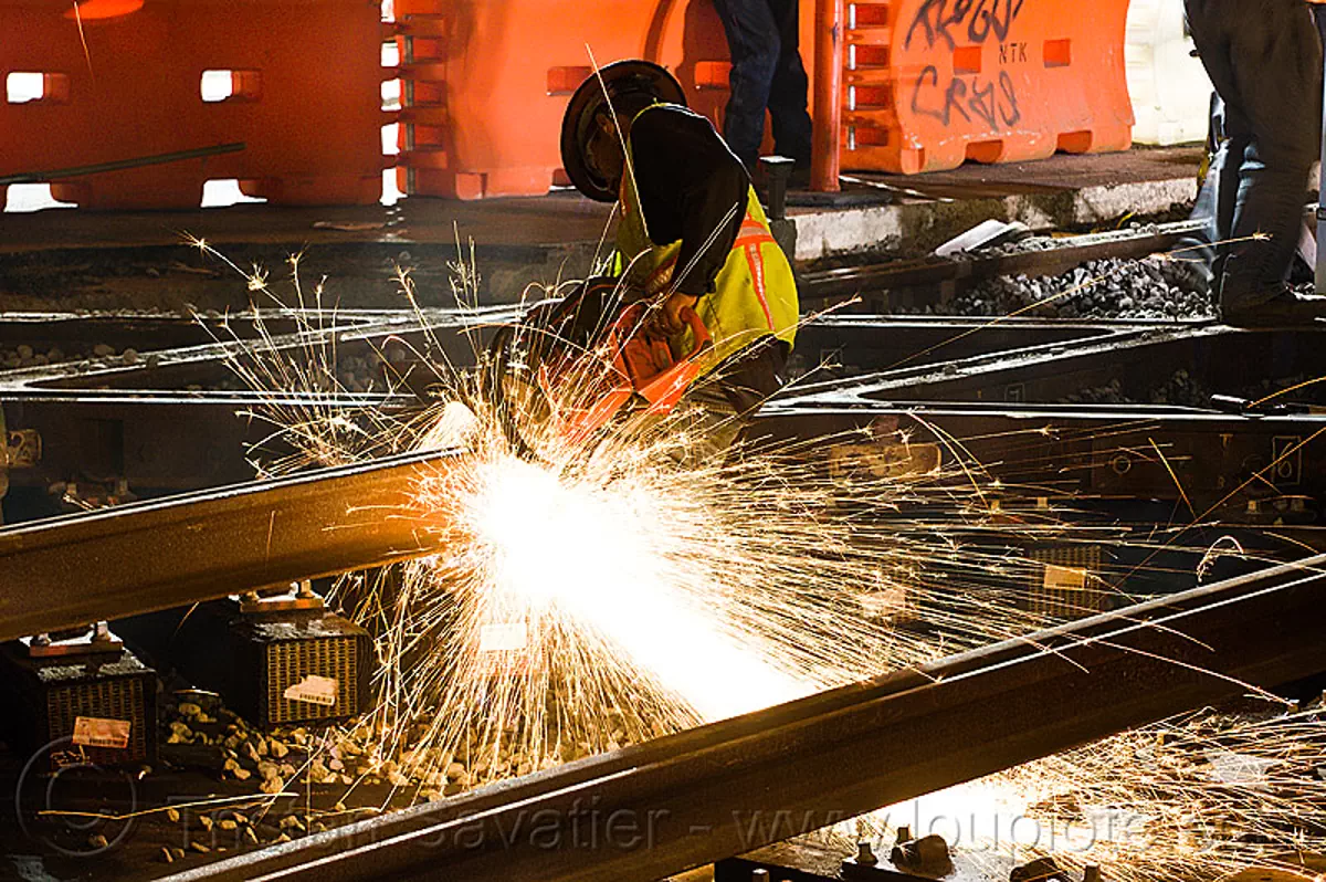 worker cutting track rail with abrasive saw, cut-off saw, diamond crossing, huskvama, k760, light rail, man, muni, night, ntk, power tool, railroad construction, railroad tracks, rails, reflective vest, safery vest, safety helmet, san francisco municipal railway, sparks, track maintenance, track work, stock photo
