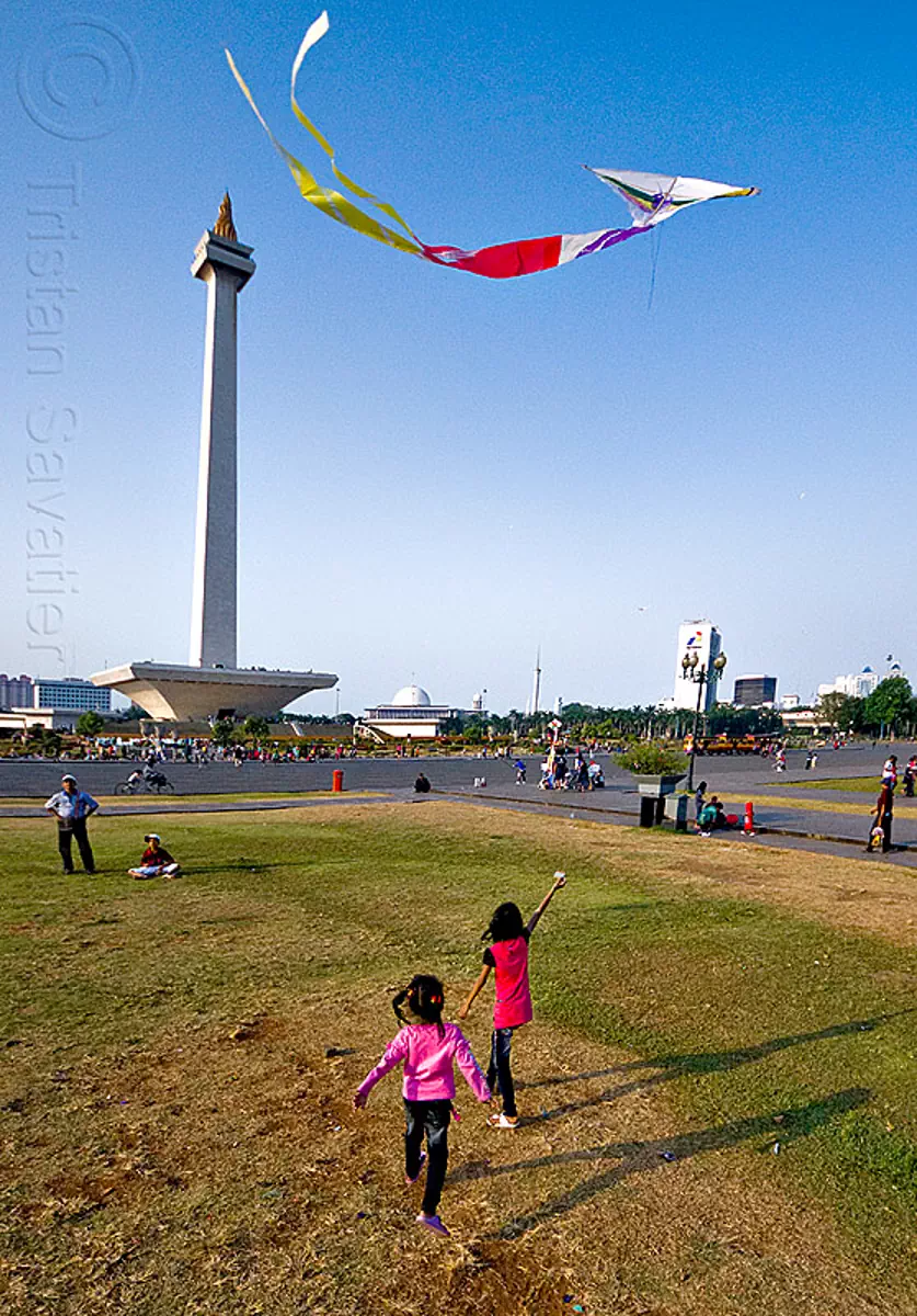 kids flying a kite near the national monument (monas) in jakarta, architecture, children, column, eid ul-fitr, girls, java, medan merdeka, merdeka square, monumen nasional, park, turf
