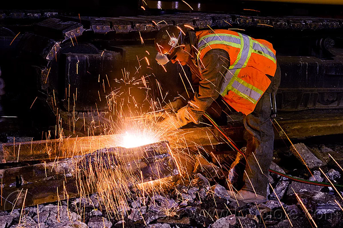 welder using cutting torch to cut a rail, demolition, light rail, man, muni, night, ntk, oxy-acetylene cutting torch, oxy-fuel cutting, railroad construction, railroad tracks, rails, reflective vest, safery vest, safety helmet, san francisco municipal railway, sparks, track maintenance, track work, welding, worker, stock photo