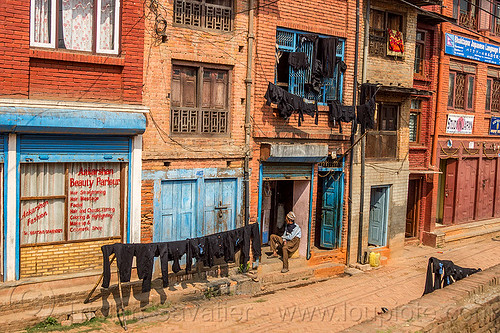 black dyed clothing drying on lines in street (nepal), bhaktapur, cloth line, drying, dyed, houses, man, sitting