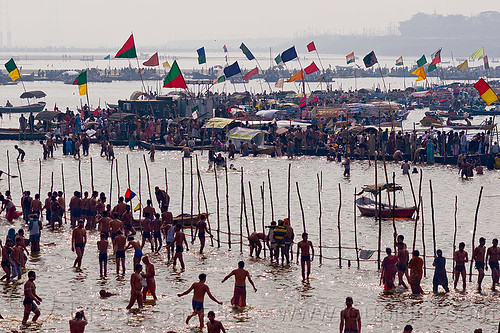 boats with flags and hindu pilgrims bathing in the ganges river at sangam - kumbh mela 2013 (india), backlight, bathing pilgrims, colored flags, crowd, dawn, fence, ganga, ganges river, hindu pilgrimage, hinduism, holy bath, holy dip, kumbh mela, moored, nadi bath, paush purnima, ritual bath, river bathing, river boats, silhouettes, triveni sangam