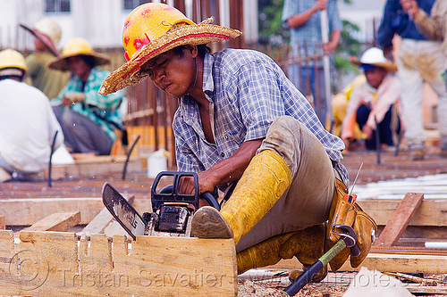 construction worker cutting timber to make concrete formwork, borneo, building construction, chainsaw, concrete forms, concrete wall forms, construction site, construction workers, formwork, lumber, malaysia, man, miri, plank, rubber boots, safety helmet, straw hat, sun hat, timber, working