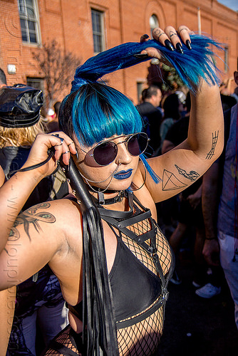 dominatrix with whip - folsom street fair 2015 (san francisco), arm tattoos, blue hair, fashion, fishnet top, leather whip, nose chain, nose piercing, nostril piercing, ponytail, sunglasses, woman