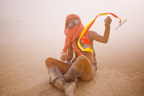 flying a mini kite, cross-legged, dust storm, flying, goggles, haboob, minah, mini kite, orange scarf, playa dust, sitting, streamer, string, whiteout, wind, woman