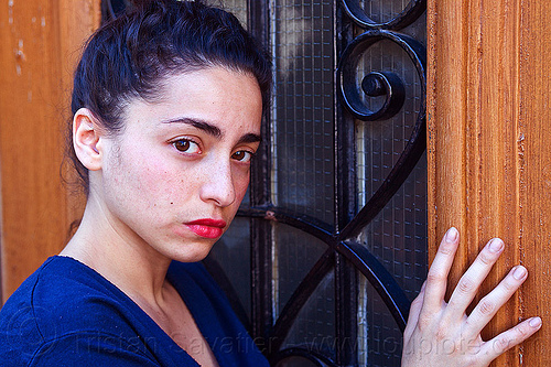italian girl with somber face, brunette, curly hair, dilve, door window, hand, house door, ironwork, italian woman, long hair, red lipstick