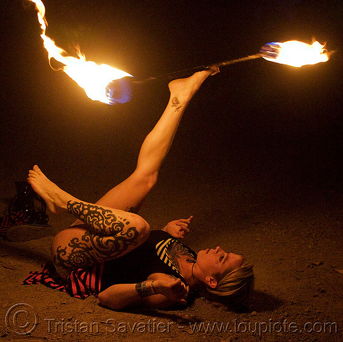 lily spinning fire staff with feet (san francisco), fire dancer, fire dancing, fire performer, fire spinning, fire staff, leg tattoo, night, spinning fire, tattooed, tattoos, woman