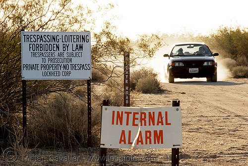 no trespassing - internal alarm - signs in mojave desert (california), car, dirt road, internal alarm, lockheed corp, loitering, no trespassing, private property, private road, signs, unpaved