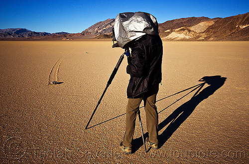 photographer with chamber camera shooting a sailing stone on the racetrack - death valley, chamber camera, death valley, dry lake, dry mud, film camera, hood, landscape, large format, man, mountains, photographer, racetrack playa, rock, sailing stones, sliding rocks, tripod