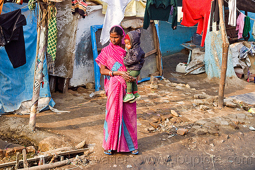 standing woman holding kid (india), baby, cloth lines, holding child, indian woman, kid, pink saree, shanty house, shanty town, toddler, village