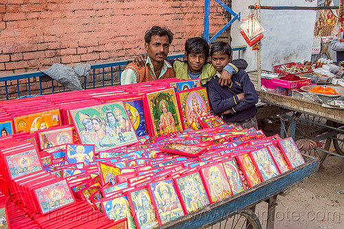 street vendor selling images of hindu gods, boys, children, daraganj, deities, father, gods, hindu pilgrimage, hinduism, holy images, kids, kumbh mela, man, merchant, religious, selling, shop, sons, stall, street market, street seller, vending, vendor