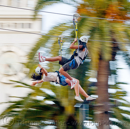 two girls riding the zip-line over san francisco, adventure, cable line, cables, campanil, climbing helmet, clock tower, embarcadero tower, ferry building, hanging, mountaineering, moving fast, palm trees, speed, steel cable, trolley, tyrolienne, urban, woman, zip line, zip wire