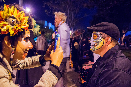 woman taking cellphone photo of man with sugar skull face paint - dia de los muertos, camera, cellphone, day of the dead, dia de los muertos, face painting, facepaint, halloween, hat, man, night, photographer, sahar, sugar skull makeup, taking photo, taking picture, woman