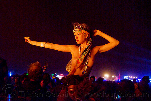 burning man - topless woman on man's shoulders, burning man at night, celebrating, crowd, dancing, goggles, topless, woman