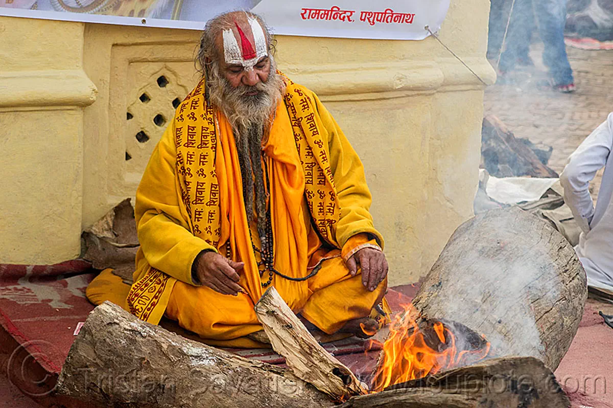baba in saffron color cloth sitting at bonfire, nepal