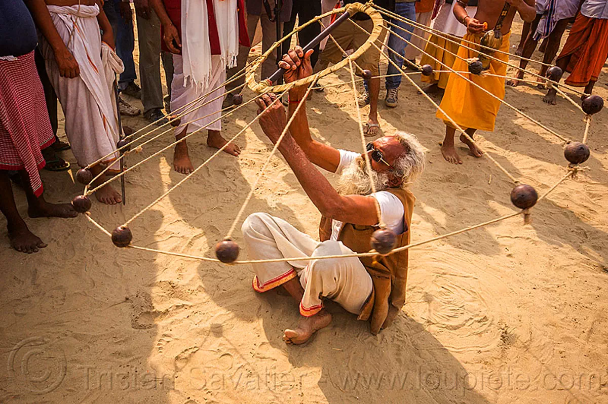 old hindu man spinning balls with ropes (india), crowd, game, hindu pilgrimage, hinduism, indian spinning balls, kumbh mela, man, metal balls, performer, ropes, sitting, spectators, white beard