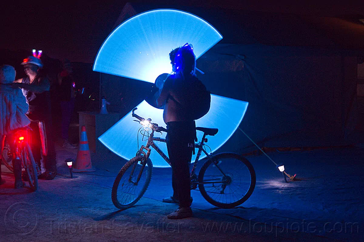 spinning light sabers, bicycle, bike, blue light, burning man, glowing, light sabers, light staff, night, silhouette