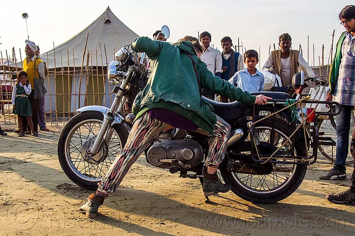 woman putting motorbike on center stand, 350cc, bun bun, hindu pilgrimage, hinduism, kumbh mela, men, motorcycle touring, motorcyclist, rider, riding, royal enfield bullet, spectators, thunderbird, watching, woman
