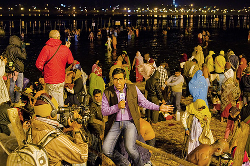 abp news live tv reporter covers the holy bath at kumbh mela 2013 (india), abp news, bathing pilgrims, broadcasting, camera, cameraman, crowd, fence, ganga, ganges river, hindu pilgrimage, hinduism, holy bath, holy dip, journalist, kumbh mela, line broadcast, men, mic, microphone, nadi bath, night, paush purnima, reporter, ritual bath, river bank, river bathing, street lights, triveni sangam, tv news, women