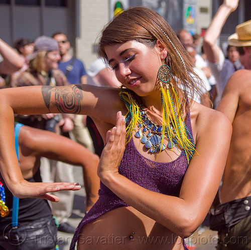 beautiful young woman dancing at street party, ariana, arm tattoo, blue stone necklace, dancing, feather earrings, gay pride festival, hands, tattoos, woman, yellow feathers