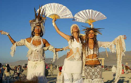 burning man - natalia, audette sophia, and pema at the silent white procession, attire, audette sophia, burning man outfit, dawn, fans, feathers, natalia, pema, stilts, stiltwalkers, stiltwalking, white morning, women