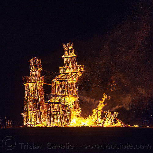 burning man - the lighthouse on fire collapses, art installation, black rock lighthouse, burning man at night, fire