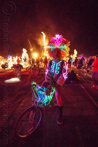 burning man - woman with glowing el-wire costume, attire, bicycle, bike, burning man at night, burning man outfit, costume, crowd, el-wire, feather headdress, feathers, glowing, japanese woman