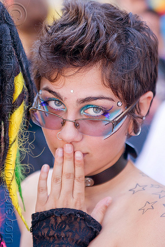 hand on mouth, bindis, emma, eye makeup, eyeglasses, eyewear, gay pride festival, gouged ears, green eyed, green eyes, nose ring, prescription glasses, shoulder tattoo, spectacles, stars tattoo, woman