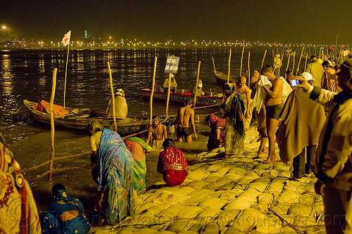 hindu pilgrims bathing in the ganges river at the sangam at night - kumbh mela 2013 (india), bathing pilgrims, crowd, fence, ganga, ganges river, hindu pilgrimage, hinduism, holy bath, holy dip, kumbh mela, men, nadi bath, night, paush purnima, ritual bath, river bank, river bathing, river boats, sand bags, street lights, triveni sangam, women, wooden poles