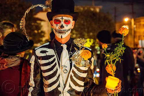 man in skeleton costume - black suit and hat - dia de los muertos, black suit, candle light, day of the dead, dia de los muertos, face painting, facepaint, feather, halloween, man, marigold flowers, necklace, night, skeleton costume, skeleton suit, skull makeup, stovepipe hat, white tie