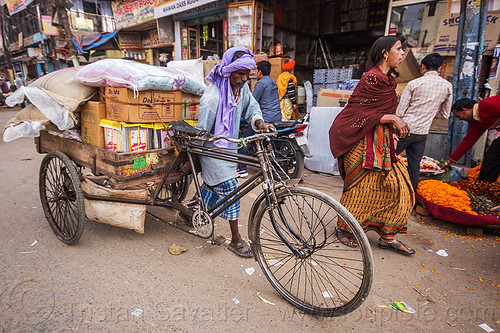 man pushing cargo tricycle with heavy load (india), bags, boxes, cargo tricycle, cargo trike, freight tricycle, freight trike, heavy, load bearer, man, moving, sacks, sarees, sari, shops, transport, transportation, transporting, varanasi, walking, wallah, woman