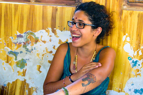 maryam and peeling paint wall, arm tattoo, bindi, bird tattoo, bracelets, djembe drum, drummer, eyeglasses, eyewear, maryam, musical instrument, necklaces, peeling paint, percussion, phoenix tattoo, prescription glasses, rishikesh, sitting, spectacles, tattoos, tongue piercing, woman