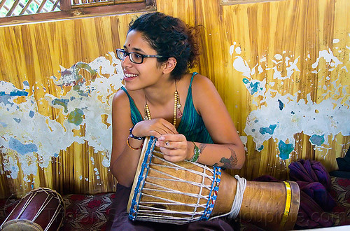 maryam with djembe drum, arm tattoo, bindi, bird tattoo, bracelets, djembe drum, drummer, eyeglasses, eyewear, maryam, musical instrument, necklaces, peeling paint, percussion, phoenix tattoo, prescription glasses, rishikesh, sitting, spectacles, tattoos, woman