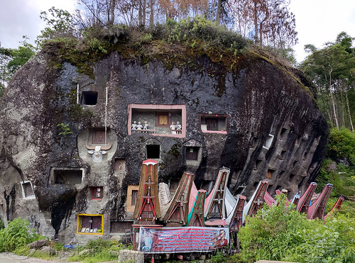 miniature tongkonan rice-barns in front of wall of toraja rock-tombs - lembang tonga riu - lo'ko mata wall, boulder, burial site, cemetery, graves, graveyard, lembang tonga riu, liang pak, lo'ko mata wall, miniature tongkonan, pa'tedong, rock tombs, tana toraja, tongkonan roof