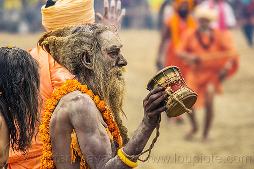 naga sadhu (hindu devotee) with ritual drum - kumbh mela (india), beard, damaru drum, dreadlocks, flower necklace, hindu pilgrimage, hindu ritual drum, hinduism, holy ash, india, maha kumbh mela, marigold flowers, men, naga babas, naga sadhus, sacred ash, sadhu, vasant panchami snan, vibhuti, walking
