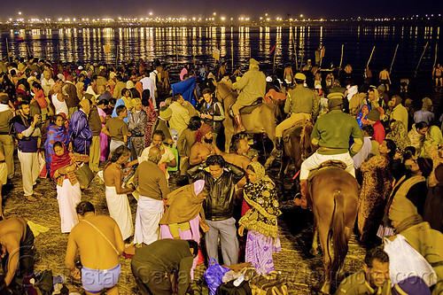 police horses patrolling the crowd of hindu pilgrims gathering at kumbh mela 2013 (india), cops, crowd control, fence, ganga, ganges river, hindu pilgrimage, hinduism, holy dip, horseback riding, kumbh mela, law enforcement, men, mounted police, night, paush purnima, pilgrims, police horses, police officers, river bank, street lights, triveni sangam, women