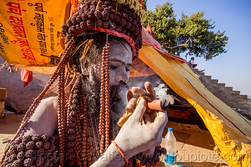 sadhu smoking chillum of weed on the ghats of varanasi (india), baba smoking chillum, beard, ganja, ghats, hindu, hinduism, man, rudraksha beads, sadhu, smoke, smoking pipe, smoking weed, tarps, varanasi, yellow
