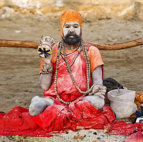 sadhu with skin covered of vibhuti sacred ash - kumbh mela 2013 (india), amputated leg, baba, bank notes, beard, coins, damaru drum, donations, hindu pilgrimage, hindu ritual drum, hinduism, holy ash, kumbh mela, man, money, necklaces, offering, paush purnima, pilgrim, red cloths, red color, rudraksha beads, sacred ash, sadhu, sitting, small drum, vibhuti, white ash, white skin