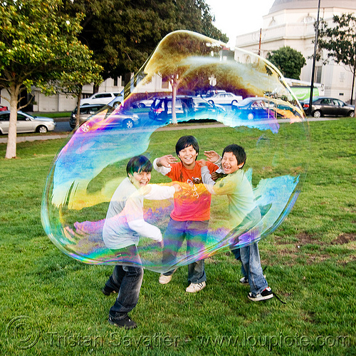 three kids behind a giant soap bubble, big bubble, children, giant bubble, iridescent, kids, lawn, park, playing, soap bubbles