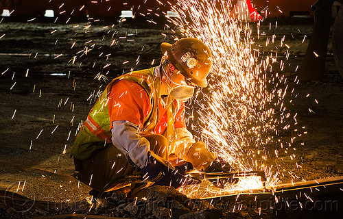 welder cutting a rail with an oxy-acetylene torch, dust mask, high-visibility jacket, high-visibility vest, light rail, man, muni, night, ntk, oxy-acetylene cutting torch, oxy-fuel cutting, railroad construction, railroad tracks, railway tracks, reflective jacket, reflective vest, safety glasses, safety helmet, safety vest, san francisco municipal railway, sparks, track maintenance, track work, welder, worker, working