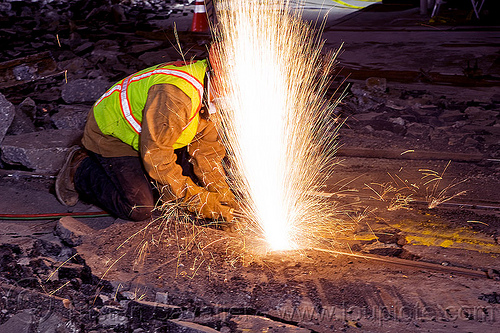 welder cutting a rail with an oxy-acetylene torch, demolition, high-visibility jacket, high-visibility vest, light rail, man, muni, night, ntk, oxy-acetylene cutting torch, oxy-fuel cutting, railroad construction, railroad tracks, railway tracks, reflective jacket, reflective vest, safety helmet, safety vest, san francisco municipal railway, sparks, track maintenance, track work, welder, welding, worker, working