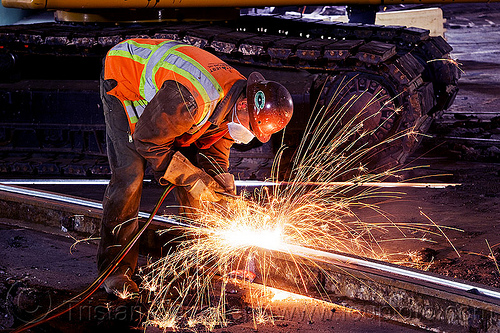 welder cutting a track rail with an oxy-acetylene torch, demolition, high-visibility jacket, high-visibility vest, light rail, man, muni, night, ntk, oxy-acetylene cutting torch, oxy-fuel cutting, railroad construction, railroad tracks, railway tracks, reflective jacket, reflective vest, safety helmet, safety vest, san francisco municipal railway, sparks, track maintenance, track work, welder, welding, worker, working