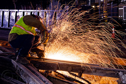 welder using cutting torch to cut a rail, demolition, high-visibility jacket, high-visibility vest, light rail, man, muni, night, ntk, oxy-acetylene cutting torch, oxy-fuel cutting, railroad construction, railroad tracks, railway tracks, reflective jacket, reflective vest, safety helmet, safety vest, san francisco municipal railway, sparks, track maintenance, track work, welder, welding, worker, working