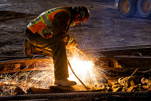 welder using cutting torch to cut a rail, demolition, high-visibility jacket, high-visibility vest, light rail, man, muni, night, ntk, oxy-acetylene cutting torch, oxy-fuel cutting, railroad construction, railroad tracks, railway tracks, reflective jacket, reflective vest, safety helmet, safety vest, san francisco municipal railway, sparks, track maintenance, track work, welder, welding, worker, working